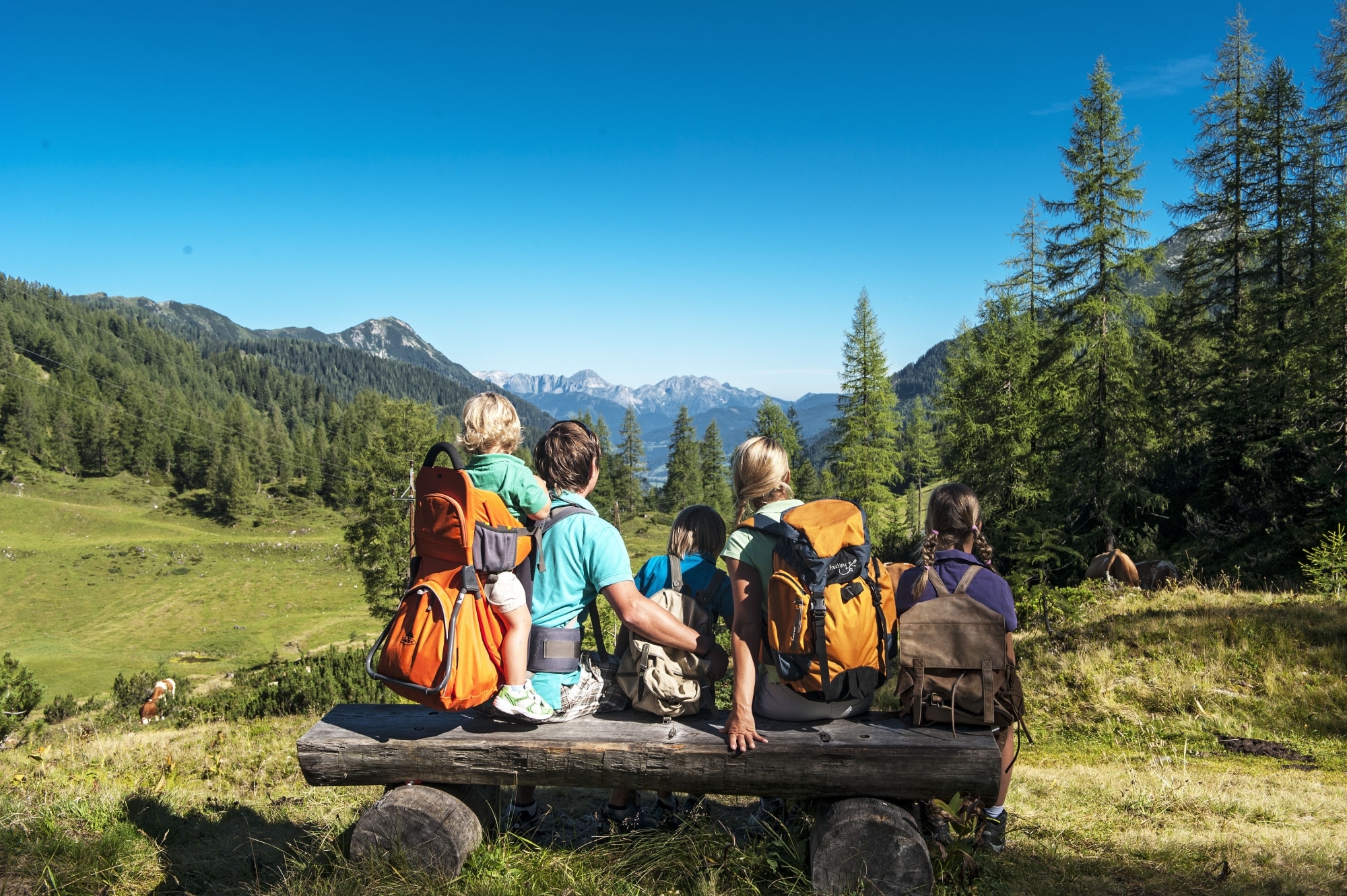 Familie macht Wander-Pause auf einer Holzbank in Zauchensee