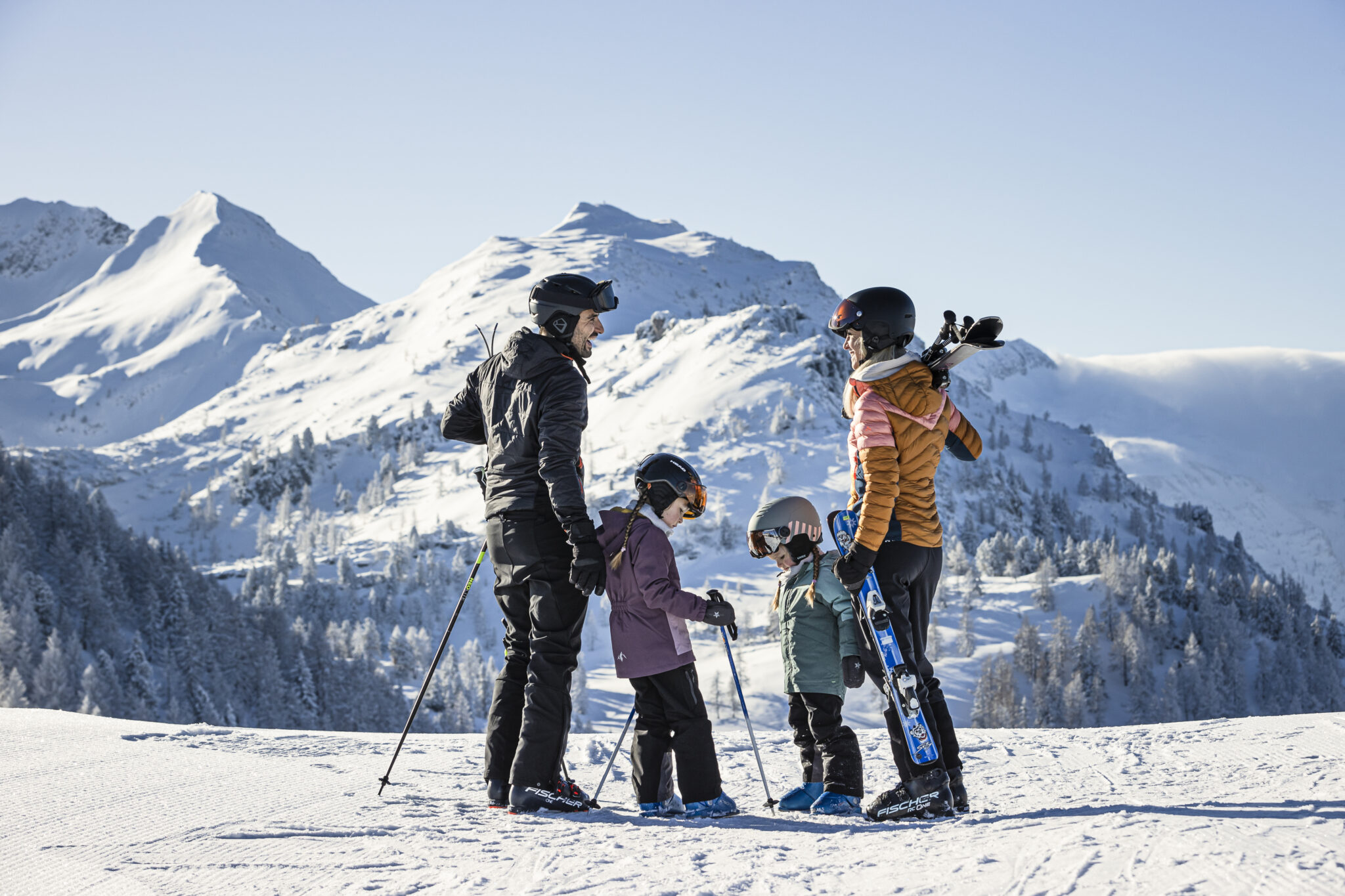 Familie mit Skiausrüstung steht auf einer schneebedeckten Piste in den Bergen. Familienhotel Zauchenseehof