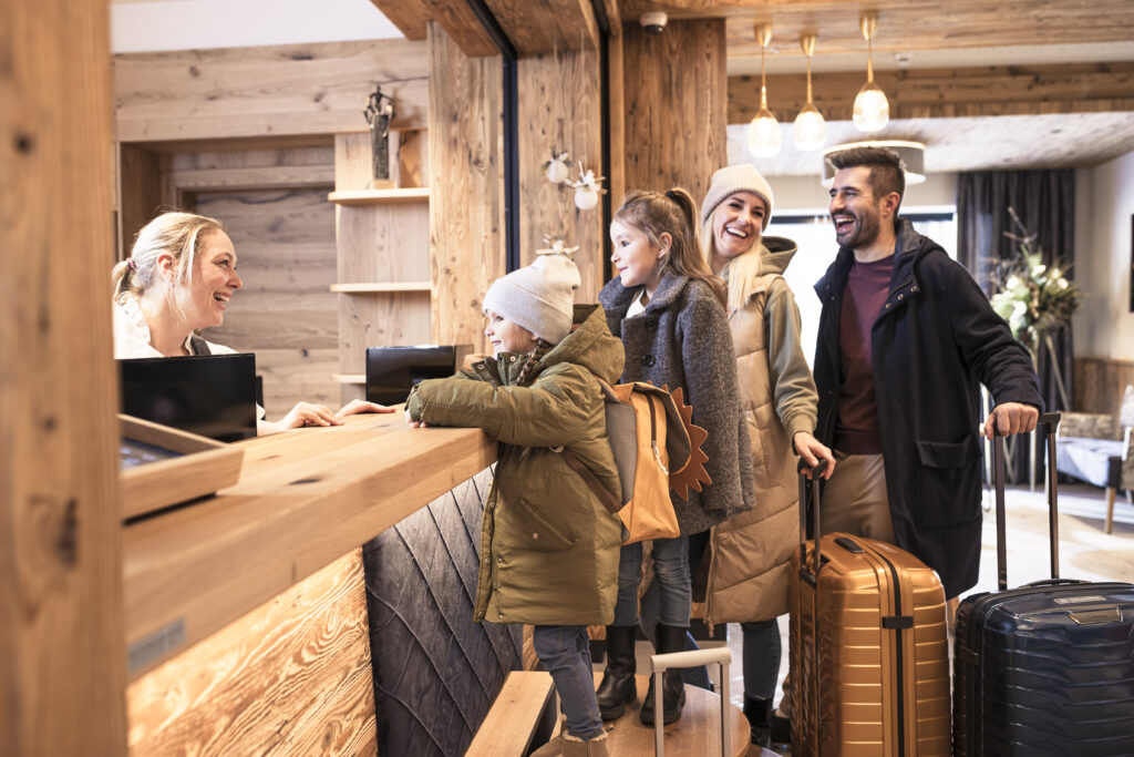 Familie mit Gepäck am Empfangstresen vom Familienhotel Zauchenseehof, während sie mit der Rezeptionistin sprechen. Familienhotel Zauchenseehof