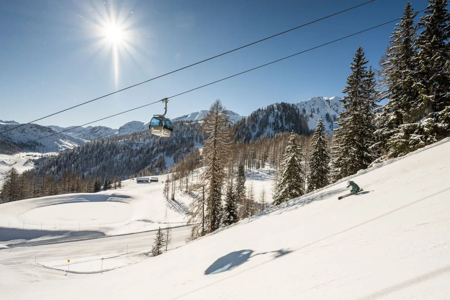 Zauchensee ski area with a cable car and snow-covered slopes under a clear sky. Zauchenseehof Family Hotel