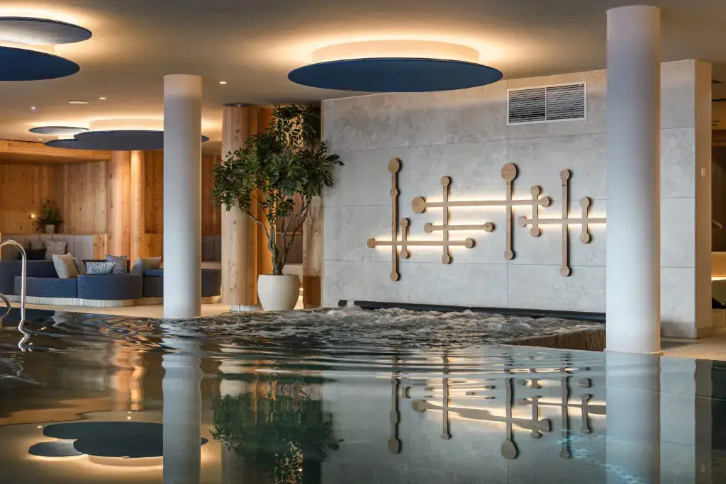 Interior view of a swimming area with modern design, water surface, and stylish wall lights at Zauchenseehof. Zauchenseehof family hotel Salzburger Land