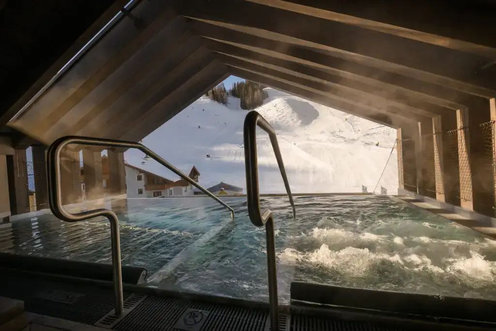Heated outdoor pool with a view of snow-covered mountains and steaming water surface at Zauchenseehof. Zauchenseehof family hotel Salzburger Land