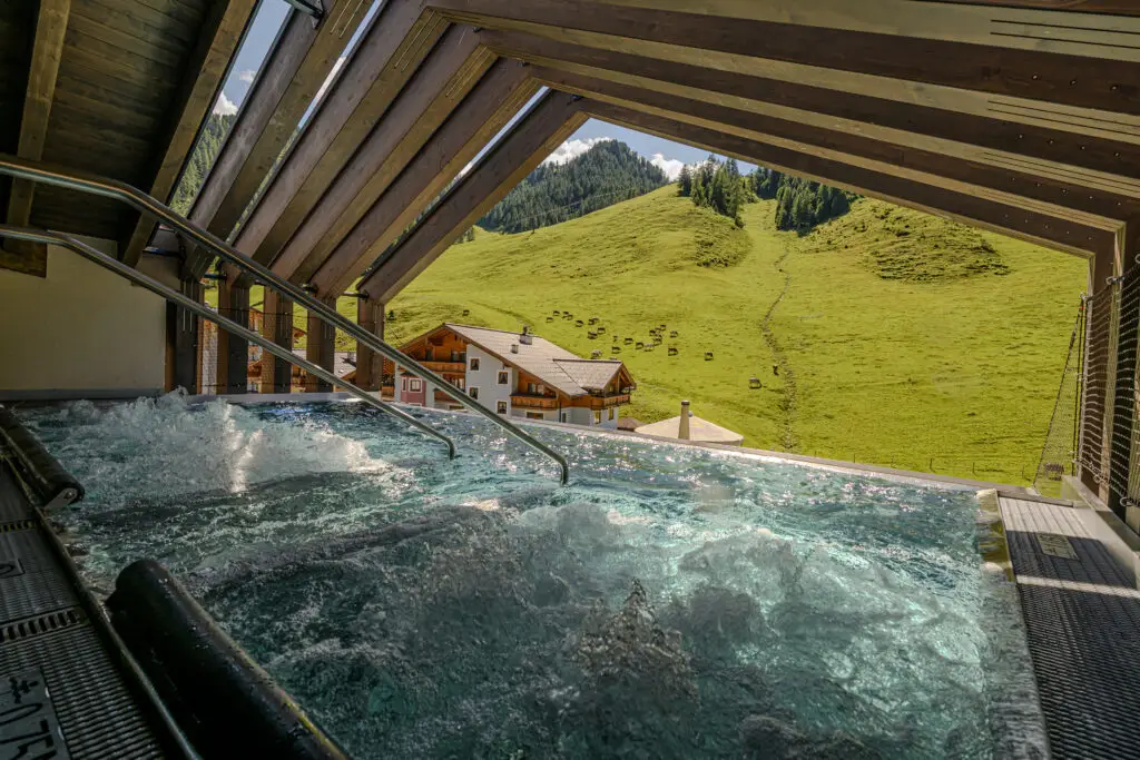 Im Spa-Bereich des Zauchenseehof sprudelt Wasser vor einer Almwiese mit H&uuml;tte und bewaldetem Berghang. Familienhotel Zauchenseehof Salzburger Land