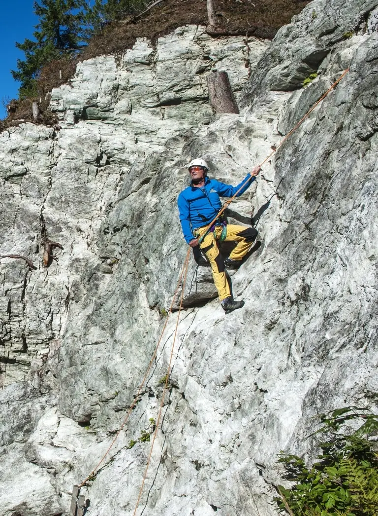 Ein Kletterer mit blauem Anorak und gelber Hose steigt am Klettersteig an der Felswand des Zauchensees empor. Familienhotel Zauchenseehof Salzburger Land